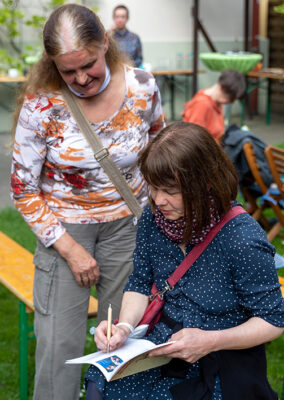 Künstlerin Susanne Janssen beim Signieren des Ausstellungskataloges “Von Anna Humpelhexe bis Zacharias Zappelbein” im LesArt-Garten