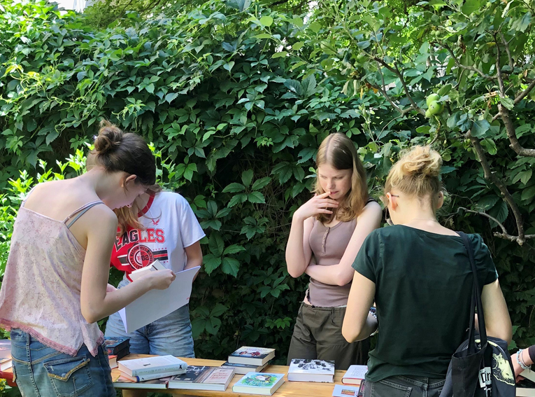 Jugendliche im LesArt-Garten, Bücher auf einem Tisch betrachtend