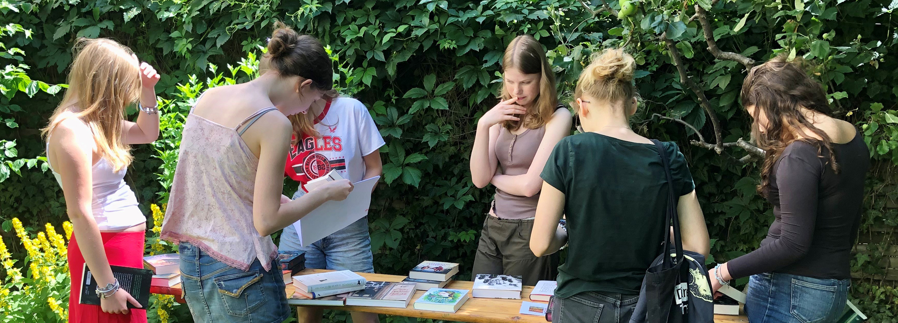 Jugendliche im LesArt-Garten, Bücher auf einem Tisch betrachtend